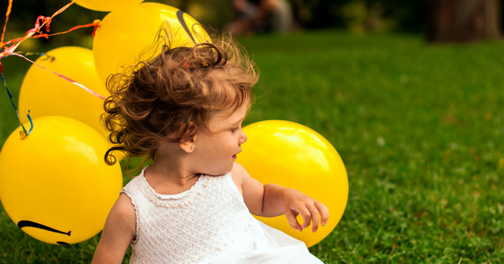 baby girl in white dress with yellow baloons