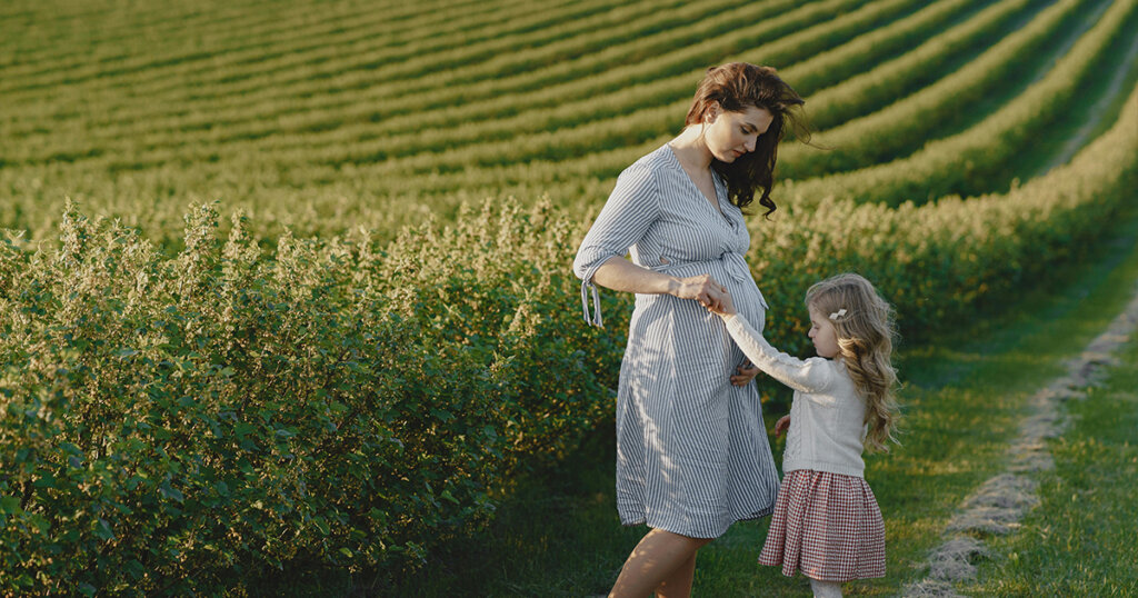 a pregnant woman with his daughter standing in beautiful green place