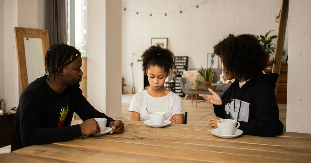 Black parents lecturing upset daughter at table