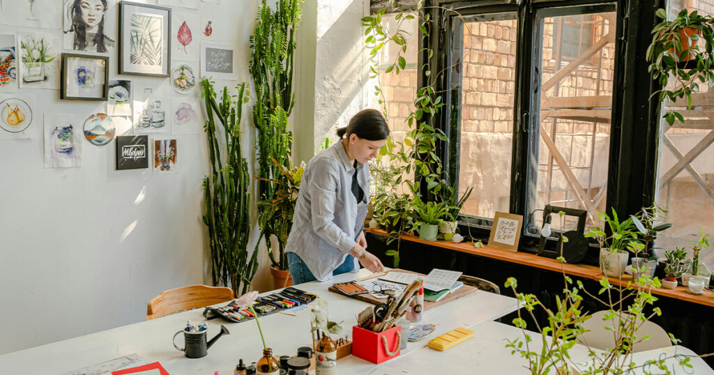 Craftswoman working with drafts at table with stationery in workshop