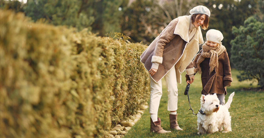 Woman and Little Girl in Brown Coat with their Small Dog on Green Grass Field