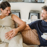 Positive man touching pregnant belly of wife in light apartment