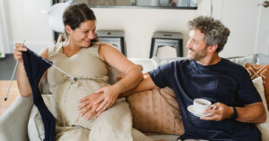 Positive man touching pregnant belly of wife in light apartment