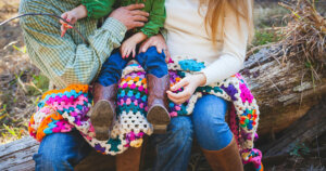 Toddler Sitting on Person's Lap While Person Sitting Also on Tree Trunk