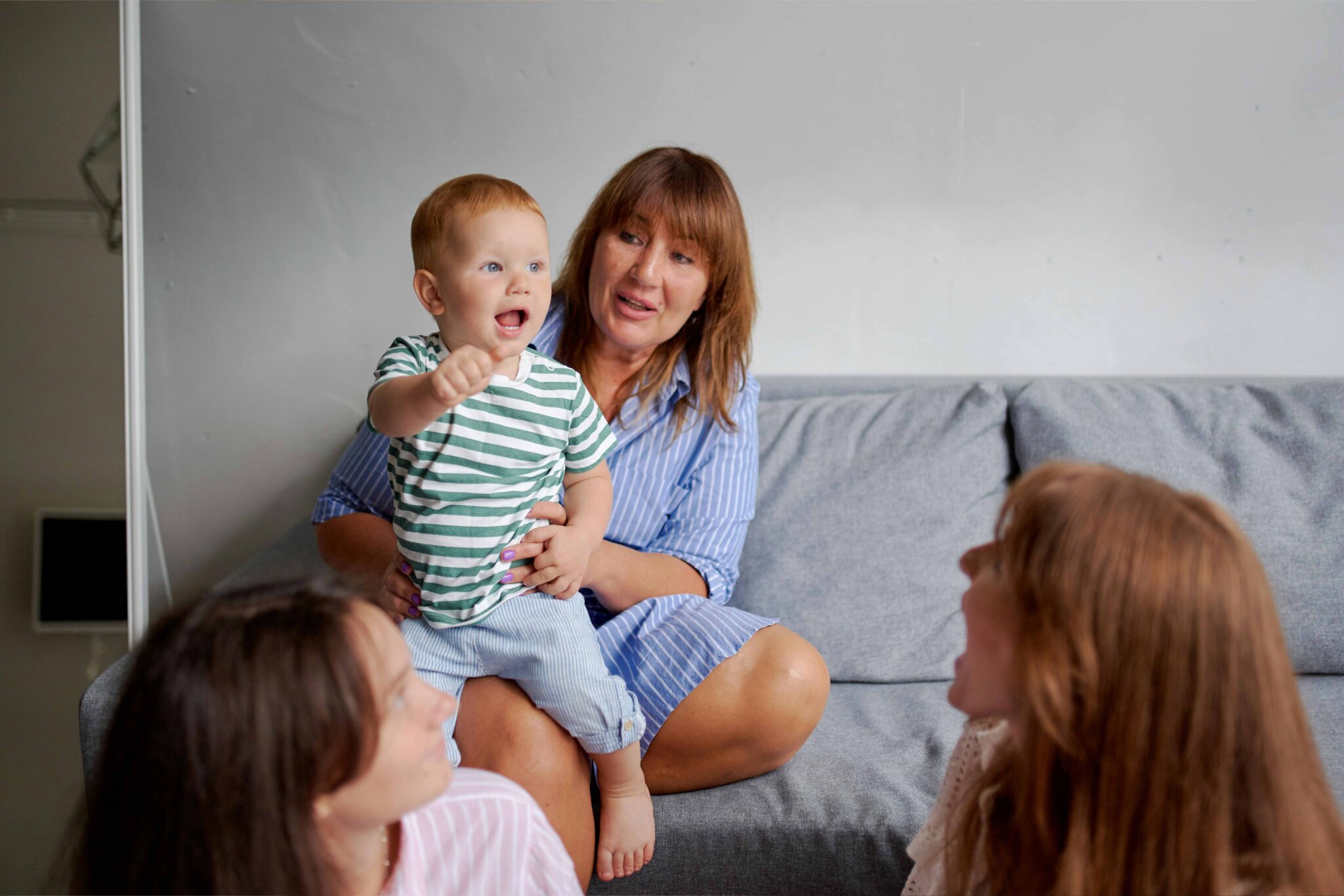 Smiling grandma with little boy on sofa near daughters