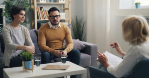 A woman and two men sitting on a couch in a living room