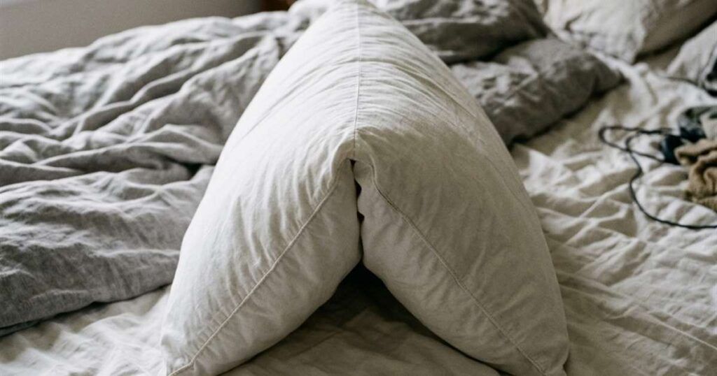 pillow-folded-in-half-lengthways-resting-on-an-unmade-bed-in-morning-light-showcasing-how-to-tell-if-you-need-a-new-pillow