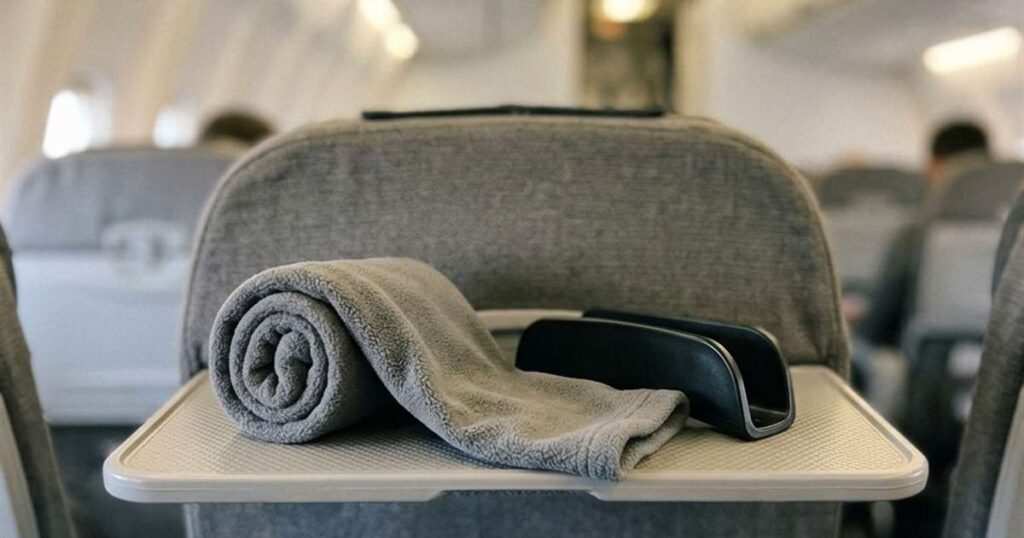 Gray fleece travel pillow partially unrolled on an airplane tray table